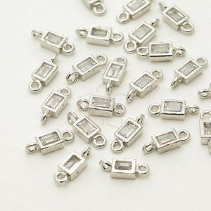 May include: Silver-toned rectangular jewelry connectors with clear rectangular crystals. Each connector has a loop on each end for attaching to other jewelry components. The connectors are scattered across a white surface.
