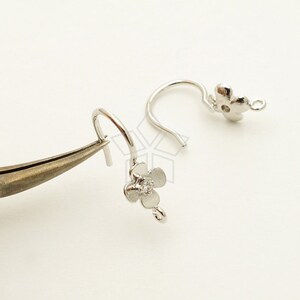 Puede incluir: Dos ganchos para pendientes de plata en forma de flor con un pequeño cristal transparente en el centro de cada flor.