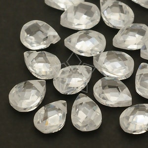 May include: A collection of clear, faceted teardrop-shaped crystal beads. The beads are arranged on a dark surface, showcasing their reflective qualities and intricate cuts. These beads are suitable for jewelry making and craft projects.