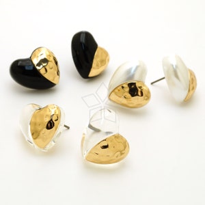 May include: A set of four heart-shaped earrings with a hammered gold finish. Two earrings are white, one is black, and one is clear.
