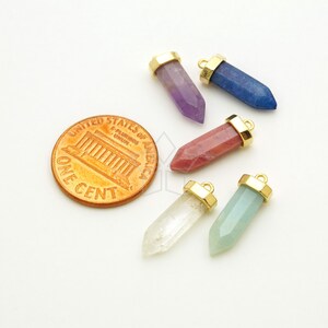 May include: Six gemstone point pendants with gold-toned caps. The gemstones are amethyst, lapis lazuli, red, clear, and green.