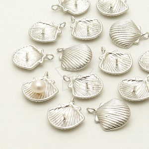 May include: A collection of silver-toned metal seashell charms with a small loop at the top for attaching to jewelry. Some of the charms have a pearl in the center.