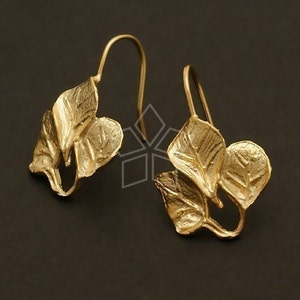 Puede incluir: Un par de pendientes de color dorado con un diseño de hojas. Cada pendiente tiene tres hojas que están conectadas a un gancho.