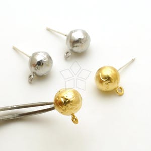 May include: Two silver and one gold earring findings with textured round balls and a loop at the bottom. The findings are on a white surface.