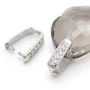 Puede incluir: Dos baúles de colgante plateados con detalles de cristal transparente. Los baúles están diseñados para sujetarse a un collar o pulsera.