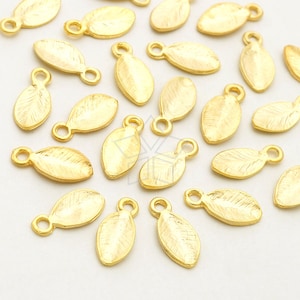 Puede incluir: Una colección de abalorios en forma de hoja de metal dorado con un bucle en la parte superior para sujetar a joyas u otras manualidades.