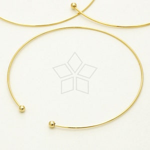 May include: A gold-toned wire choker necklace with two small round balls at the ends.