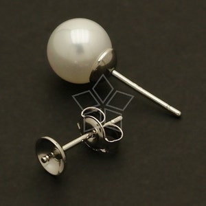 May include: A pair of silver earring posts with a white pearl on one post. The pearl is round and smooth.
