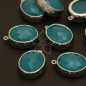 May include: Teal blue oval-shaped gemstone pendants with silver settings. The pendants have a hammered texture and a loop for attaching to a chain or cord.