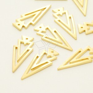 May include: A group of gold-colored metal arrowhead shapes with a geometric design. The arrowheads are arranged in a random pattern on a white surface.