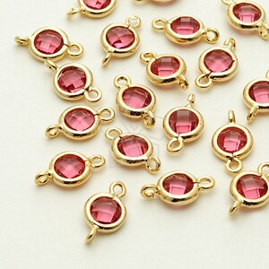 May include: A group of pink crystal connectors with gold-toned metal loops. The connectors are scattered on a white surface.