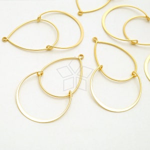 May include: Gold-toned metal hoops with a teardrop shape. The hoops are double-layered, with a smaller hoop inside a larger hoop.