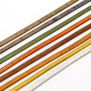 May include: An assortment of colorful leather strips in various shades, including brown, green, orange, and gold. The strips have textured surfaces and are arranged diagonally against a white background. Ideal for jewelry making or crafting.