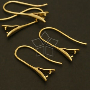 May include: Four gold-toned earring hooks with a loop at the top and a small, flat, pointed end. The hooks are arranged in a staggered pattern on a black surface.