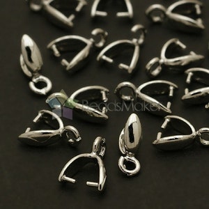 Op de afbeelding: Zilverkleurige metalen sluitingen voor het maken van sieraden. De sluitingen zijn gevormd als een kleine lus met een puntig uiteinde. Ze liggen verspreid op een zwart oppervlak.