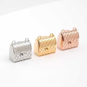 May include: Three miniature handbag charms in silver, gold, and rose gold. Each charm has a quilted pattern and a clasp closure. The charms have small loops at the top for attaching to jewelry or other crafts.