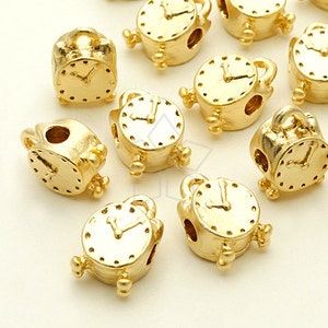 May include: A collection of gold-tone metal alarm clock charms. The charms are detailed with clock faces and hands.
