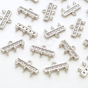 May include: Silver-toned metal connector with three loops and a row of clear cubic zirconia stones. The connector is designed for jewelry making.