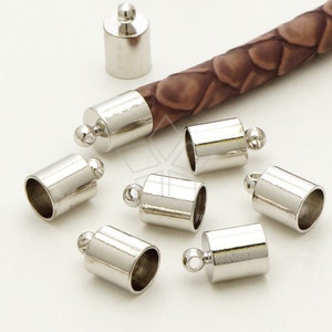 May include: Silver metal end caps for cord or rope. The caps have a round top and a hole for threading cord. The caps are shown on a brown cord.