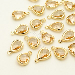May include: A collection of gold teardrop-shaped charms with clear crystal accents. The charms have a loop at the top for attaching to jewelry or other crafts.