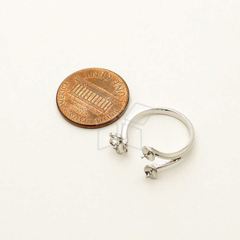 May include: Silver ring with two prongs for attaching pearls or other gemstones. The ring is shown next to a US penny for size comparison.