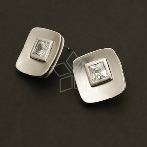 Può includere: Un paio di orecchini d'argento con un design quadrato. Ogni orecchino presenta un cristallo trasparente di forma quadrata al centro.