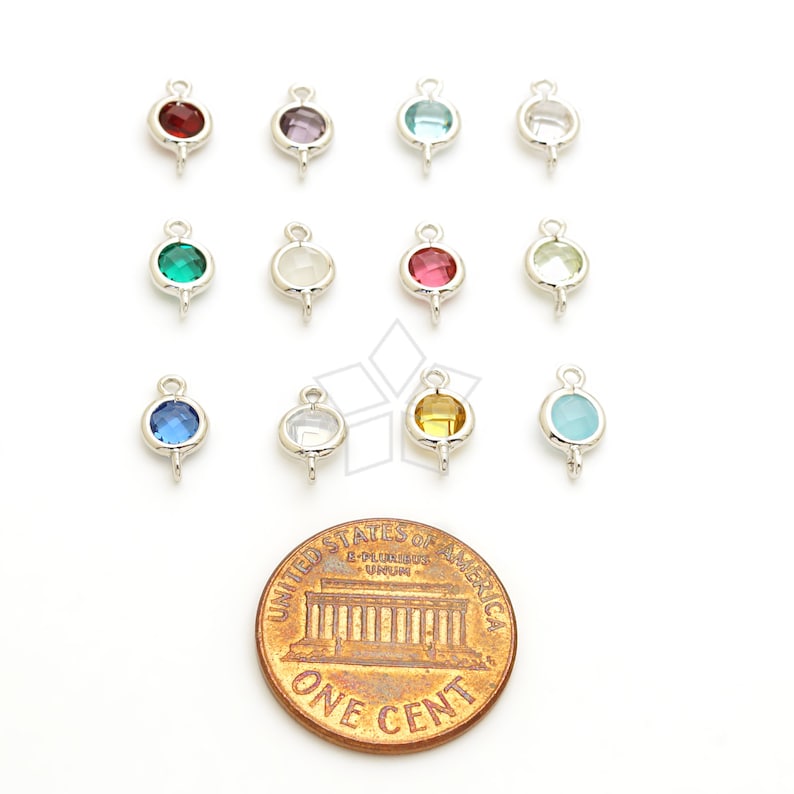 May include: A collection of small, silver-toned jewelry charms with various colored gemstones, including red, purple, blue, and green. A penny is included for size reference. The charms have a loop at the top and a small post at the bottom.