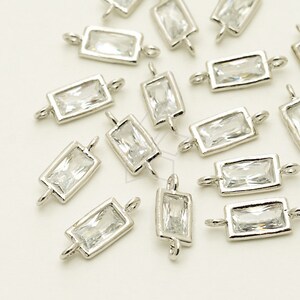 May include: A group of silver-toned rectangular pendant charms with clear crystal accents. Each charm has a loop on either side for attaching to a chain or cord.