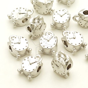 Puede incluir: Encantos de reloj despertador de metal plateado con un agujero en el centro. Los encantos tienen aproximadamente 2,5 cm de diámetro y tienen una esfera de reloj detallada con manecillas.