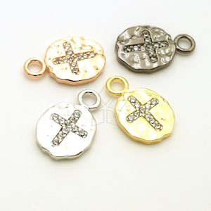 May include: Four silver, gold, rose gold, and black charm pendants with a cross design. Each pendant has a small loop at the top for attaching to a chain or bracelet. The cross is decorated with clear rhinestones.