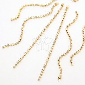 Puede incluir: Un conjunto de seis cadenas de strass doradas con piedras transparentes. Las cadenas son de diferentes longitudes y están dispuestas en un patrón aleatorio sobre un fondo blanco.