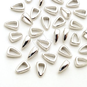 Puede incluir: Un grupo de baúles de colgantes triangulares plateados con una punta puntiaguda. Los baúles están dispersos sobre una superficie blanca.