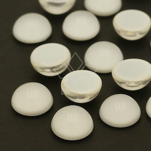 Puede incluir: Una colección de cabujones blancos en forma de media esfera con un acabado brillante. Las superficies lisas y redondeadas reflejan la luz. Estos suministros de artesanía son ideales para la creación de joyas.