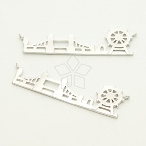 May include: Two silver charms, one depicting the London Eye Ferris wheel and the other depicting Tower Bridge. Both charms have a loop for attaching to a necklace or bracelet.