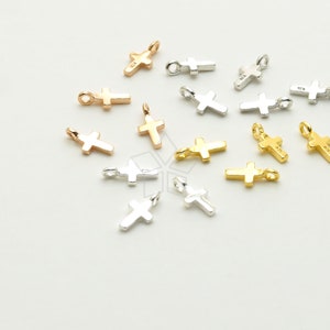 Può includere: Una collezione di piccoli ciondoli a forma di croce in argento, oro e oro rosa. I ciondoli sono tutti della stessa dimensione e forma, e hanno un design semplice ed elegante.