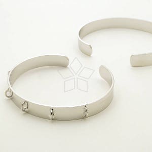Puede incluir: Dos pulseras de plata, una con un diseño simple y la otra con múltiples anillos decorativos.