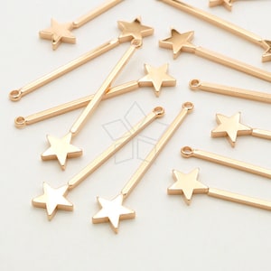 May include: Gold-toned metal star charms with a long, thin, straight bar attached to the top point of the star. The charms are scattered on a white surface.