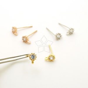 Puede incluir: Tres pares de cierres de pendientes con un cristal transparente en el centro. Los cierres son de oro, oro rosa y plata.