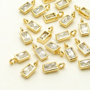 Könnte beinhalten: Eine Sammlung goldfarbener rechteckiger Anhänger mit klaren Kristall-Akzenten. Jeder Anhänger hat eine Öse zum Anbringen an Schmuck oder andere Bastelarbeiten.