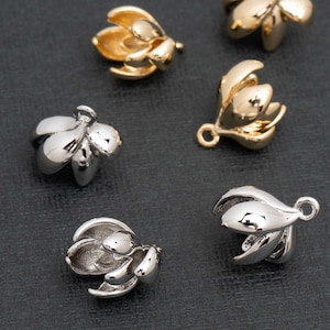 May include: Close-up of several flower-shaped jewelry components in gold and silver tones. Each component has a loop for attaching to other jewelry pieces. The petals are curved and detailed, giving a realistic appearance.