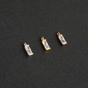 May include: Three silver, gold, and rose gold charms with clear rectangular stones. The charms are for jewelry making.