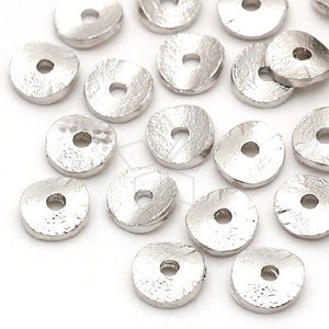 Könnte beinhalten: Eine Sammlung silberfarbener Metall-Spacer-Perlen. Die Perlen sind flach und rund mit einem Loch in der Mitte. Sie haben eine leicht strukturierte Oberfläche.