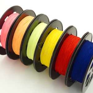 May include: Six spools of colorful thread, wound on black plastic bobbins. The thread colors are pink, orange, yellow, green, yellow, red, and blue.