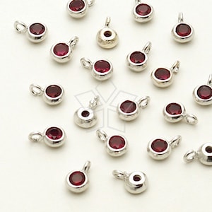 May include: A collection of 20 silver-toned charms with red crystal accents. Each charm features a small loop for attaching to jewellery or other crafts.