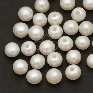 May include: A collection of white pearl beads, each with a smooth, round shape. The beads are arranged in a random pattern on a black surface.