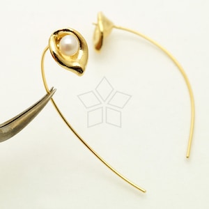 May include: Gold hoop earrings with a small pearl in a gold flower-shaped setting.