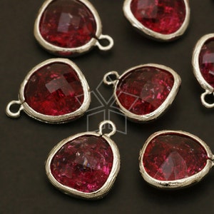 May include: Close-up of several faceted, heart-shaped, ruby-red gemstone pendants with silver-colored, textured bezels. Each pendant has a small loop at the top for attaching to a chain or other jewelry component. The background is dark.