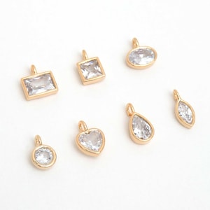 May include: An assortment of gold-tone pendants in diverse shapes, such as square, oval, teardrop, and heart, each set with a clear, faceted gemstone. These pendants are suitable for jewellery making or crafting projects.