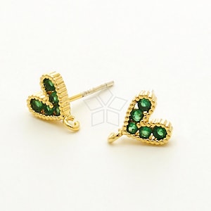 May include: A pair of gold heart-shaped earrings with green gemstones. The earrings have a post back and a small loop for attaching a charm.