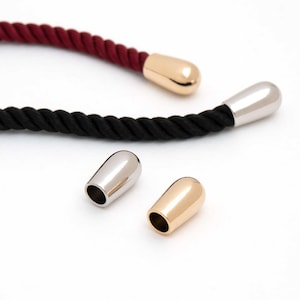 May include: Close-up of two ropes with metal end caps. One rope is black, the other is burgundy. Two metal end caps are silver, and one is gold. The end caps are teardrop-shaped and have a smooth, polished finish.